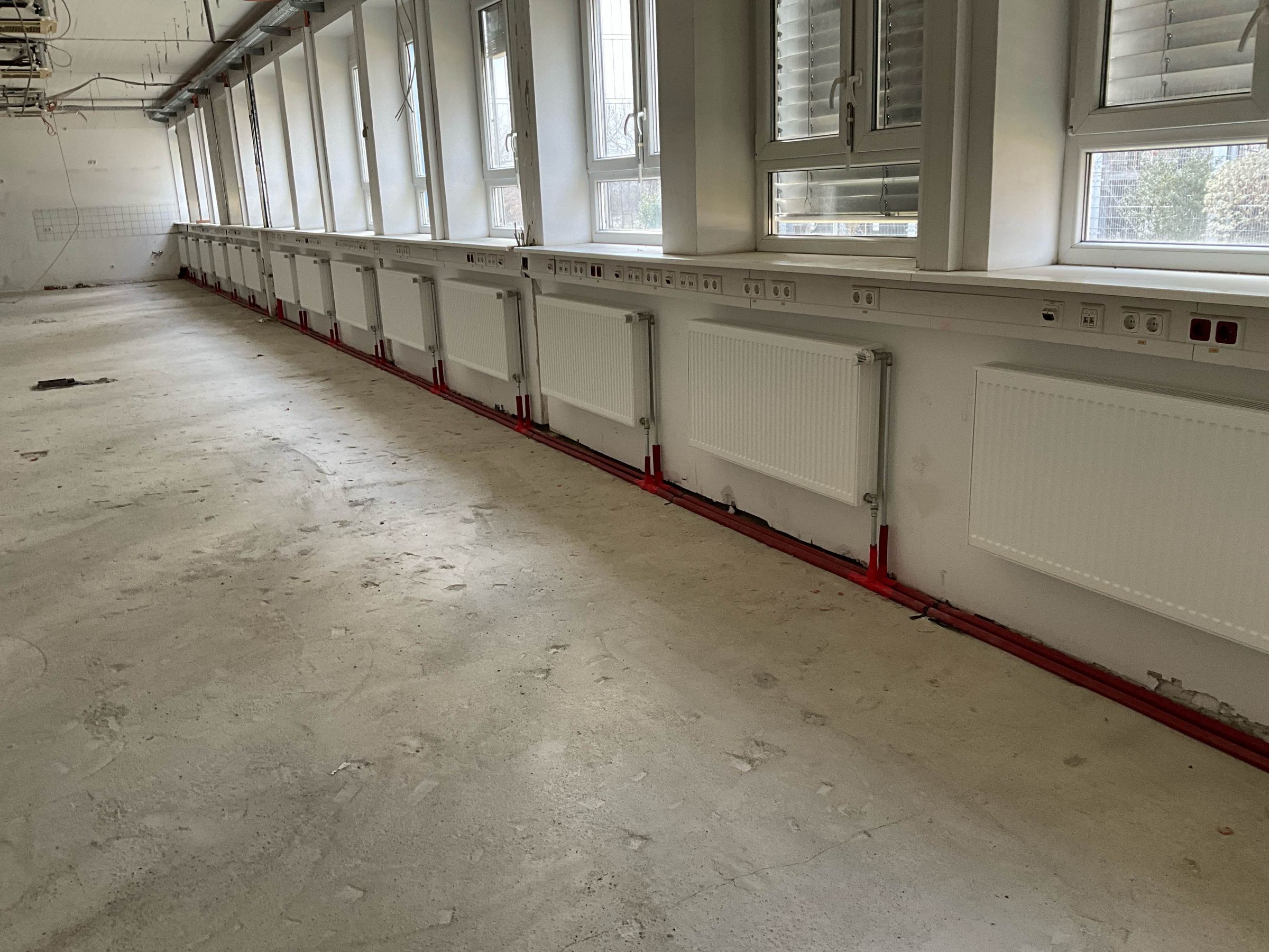 Fluchtende Reihe neu montierter Heizkörper entlang der Fensterfront eines Bürogeschosses